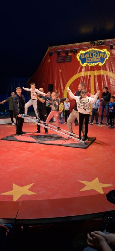 Zirkusvorstellung mit Artisten, die auf einem Seil balancieren. Zuschauer genießen die Aufführung.