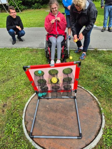 Eine Rollstuhlfahrerin spielt mit anderen Menschen ein Spiel im Freien.
