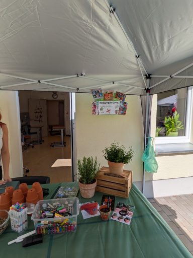 Markttisch unter einem Zelt mit Pflanzen, Bastelmaterialien und einem bunten Schild.
