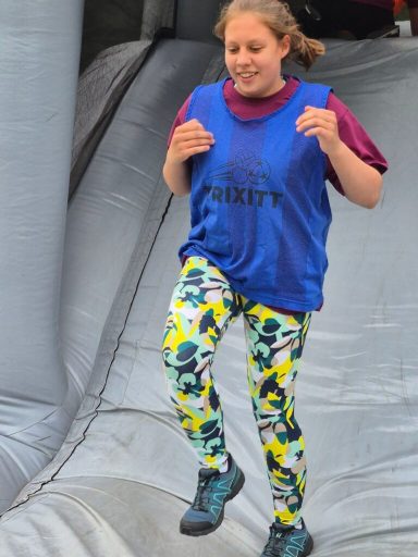 Eine Person springt auf einer Rutsche, trägt bunte Leggings und ein blaues Shirt.