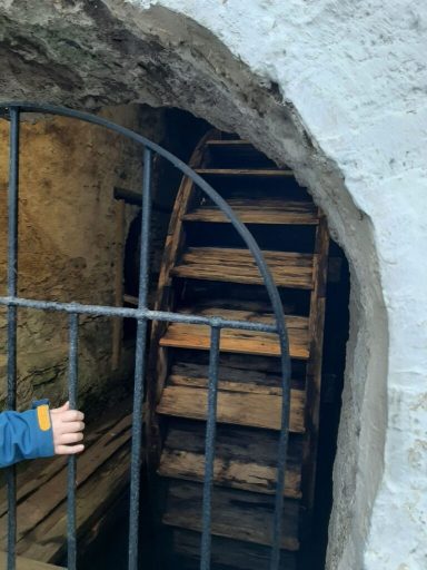 Holztreppe hinter einem Gittertor in einem alten Gebäude.