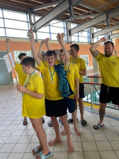 Jugendliche in gelben T-Shirts feiern mit Medaillen und erhobenen Händen.
