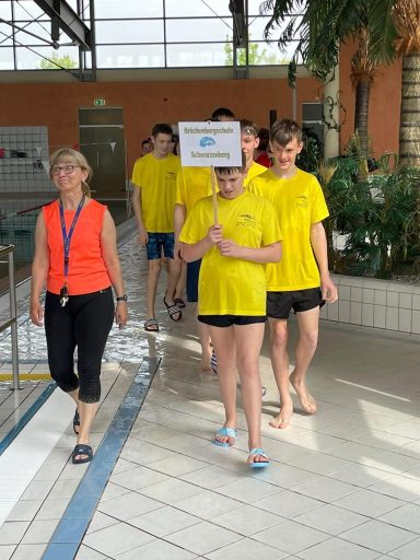Grupp von Schwimmern in gelben T-Shirts, die einer Aufwärmübung folgen.