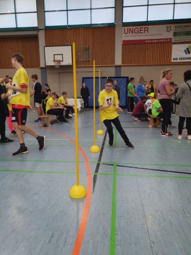 Junge in gelbem Shirt überwindet Hindernisse in einer Sporthalle.