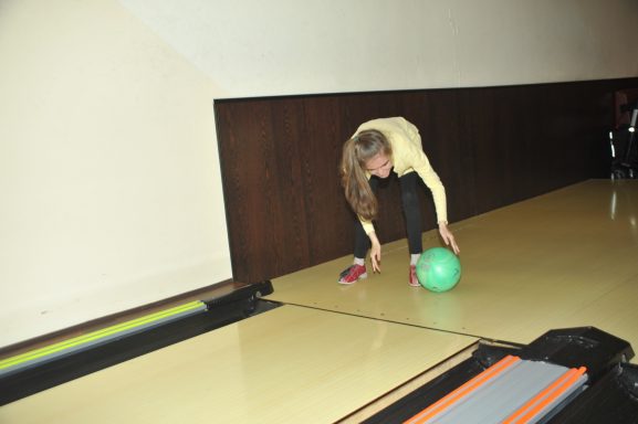 Eine Person beugt sich, um eine grüne Bowlingkugel zu greifen.