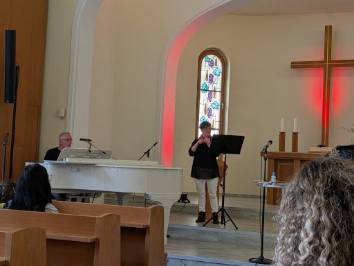 Frau singt am Mikrofon, begleitet von einem Pianisten in einem Kirchenraum.