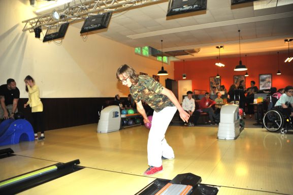 Person wirft eine Bowlingkugel auf die Bahn in einem belebten Bowlingcenter.