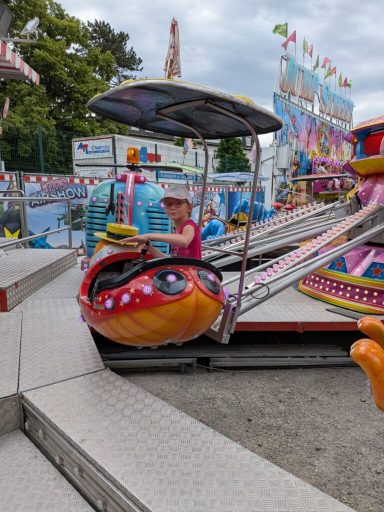 Ein Kind sitzt in einem bunten Fahrgeschäft auf einem Jahrmarkt.