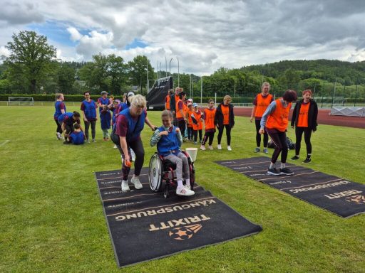 Gruppensportereignis mit Teilnehmern in Rollstühlen und orangefarbener Kleidung auf einem Sportplatz.