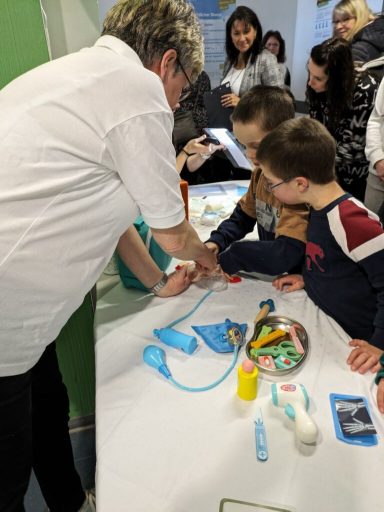 Ein Lehrer zeigt Kindern verschiedene Alltagsgegenstände auf einem Tisch.