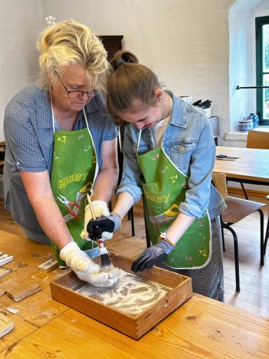Zwei Frauen arbeiten gemeinsam an einem Tisch und bereiten Materialien in einer Holzschachtel vor.