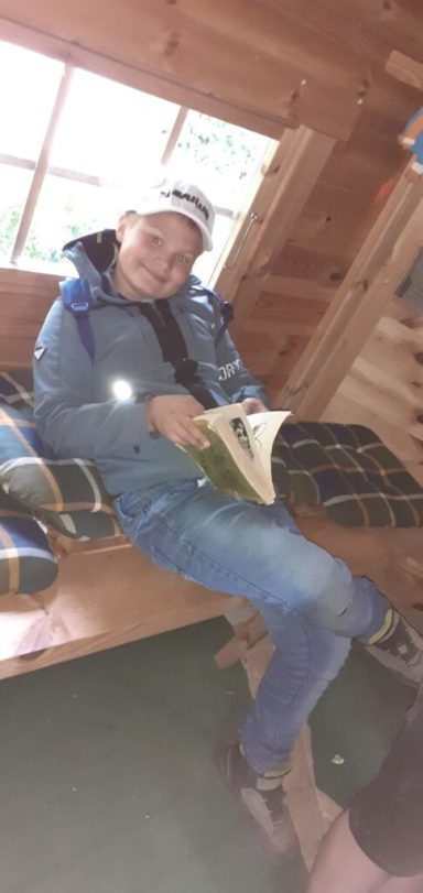 Junger Mann in einer Hütte, der ein Buch auf einer Holzbank liest.