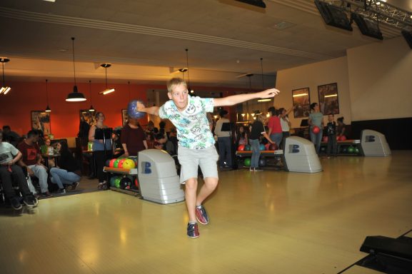 Junger Mann wirft eine Bowlingkugel in einer belebten Bowlingbahn.
