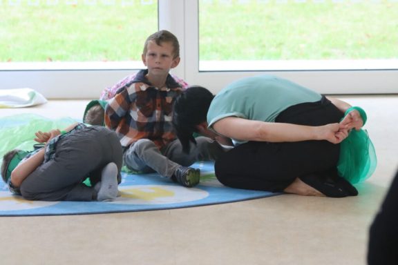Kinder spielen auf einer Matte, während ein Erwachsener sich zu ihnen beugt.