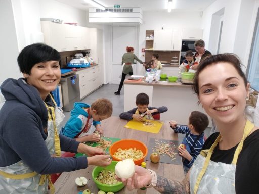 Zwei Frauen und Kinder arbeiten gemeinsam in einer modernen Küche an Essensvorbereitungen.