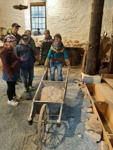 Eine Person schiebt eine Schubkarre mit Sand, umgeben von vier anderen Personen.