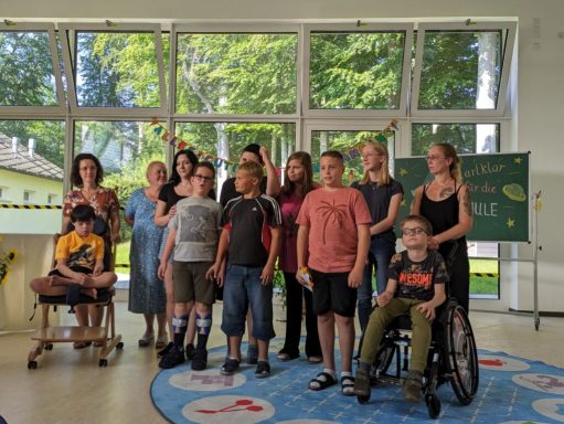 Gruppe von Personen, die in einem lichtdurchfluteten Raum stehen und zusammenlächeln.