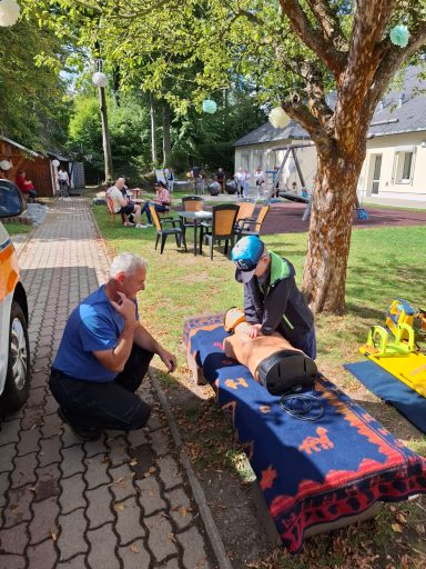 Ein Mann kniet neben einer liegenden Person auf einer Decke im Freien.