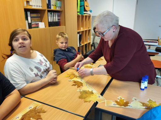 Eine Frau befestigt Herbstblätter an einer Schnur, während Kinder zuschauen.