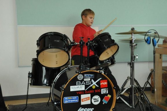 Ein Junge in rotem Shirt spielt leidenschaftlich Schlagzeug.