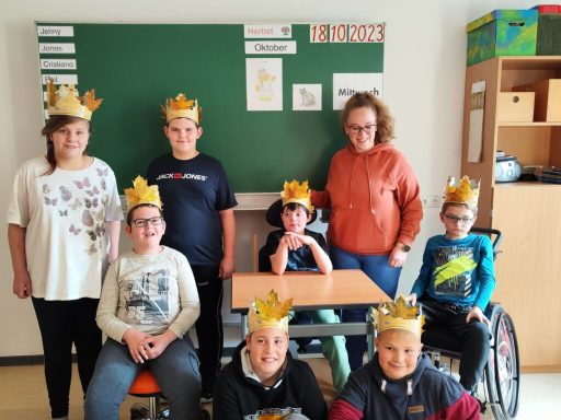 Gruppenfoto von Kindern mit Kronen, die in einem Klassenraum stehen und sitzen.