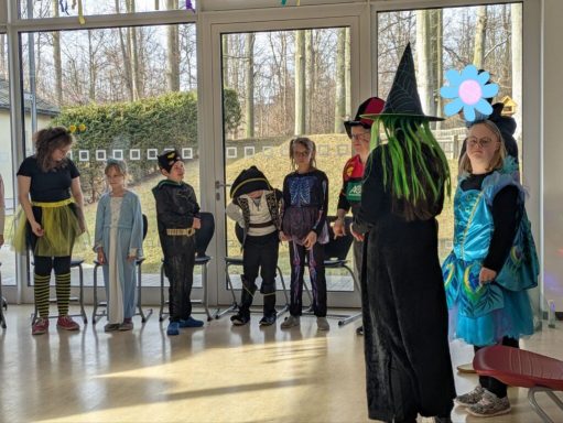 Kinder in Kostümen stehen in einem Raum, einige mit Hüten und dekorativen Accessoires.