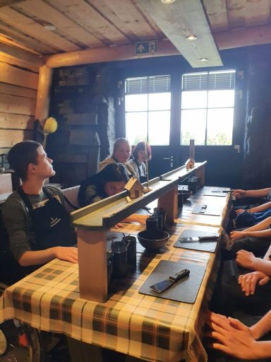 Fünf Personen sitzen an einem Tisch in einem rustikalen Raum mit Fenstern.