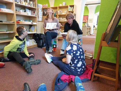 Vier Personen sitzen in einem Raum und diskutieren, während ein Kind am Boden sitzt.