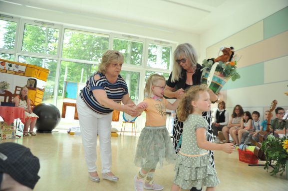 Zwei Kinder tanzen mit zwei Erwachsenen in einem hellen Raum, umgeben von festlicher Dekoration.