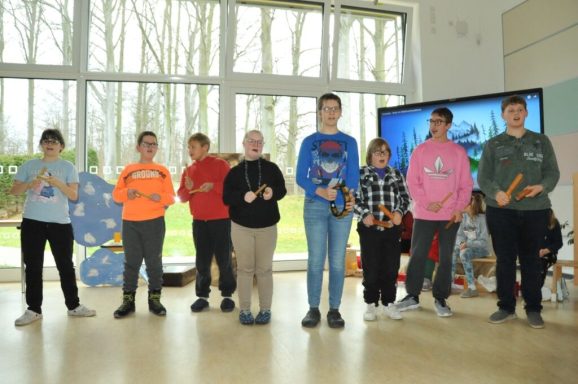 Gruppe von Jugendlichen steht in einer Reihe, hält Musikinstrumente und lächelt.