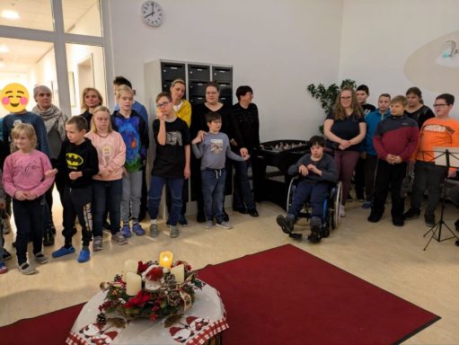 Eine Gruppe von Kindern und Erwachsenen steht in einem Raum mit festlicher Dekoration.