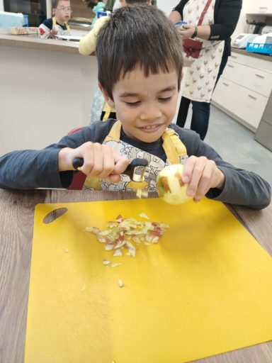 Ein Junge schält einen Apfel auf einem gelben Schneidebrett in einer Küche.