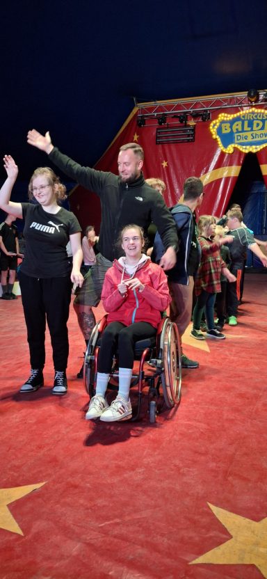 Menschen in einem Zirkuszelt, einige in Rollstühlen, andere stehen.