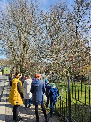 Personen betrachten einen mit bunten Ostereiern geschmückten Baum im Frühling.