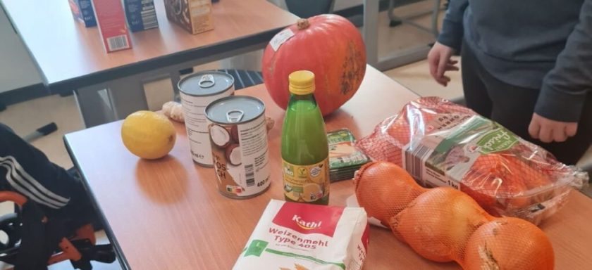 Ein Tisch mit Lebensmitteln: Kürbis, Karotten, Zitrone, Dosen und Saftflasche.