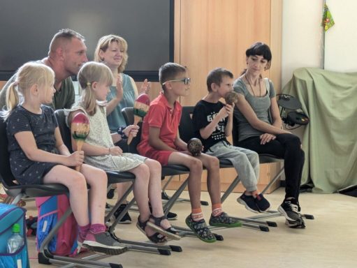 Gruppensitzung von Kindern und Erwachsenen mit Spielzeug und Snacks in einem hellen Raum.