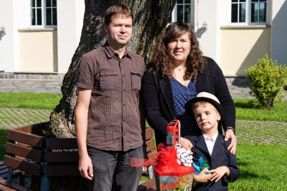 Familie steht vor einem Baum, der Junge trägt einen Anzug und hält ein Spielzeug.