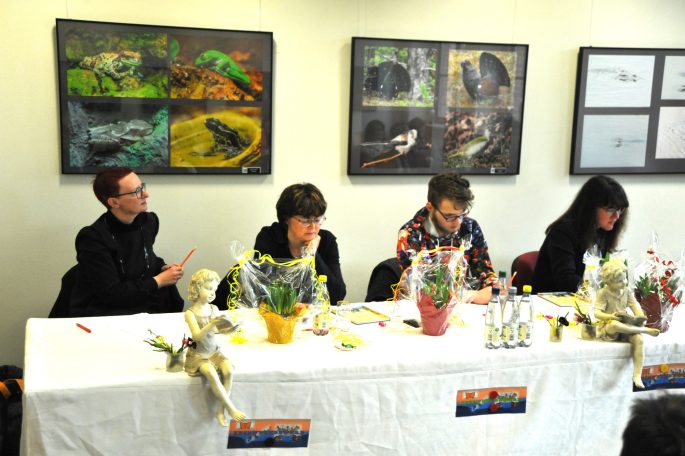 Vier Personen an einem Tisch mit dekorierten Töpfen und Pflanzen, im Hintergrund Kunstwerke.