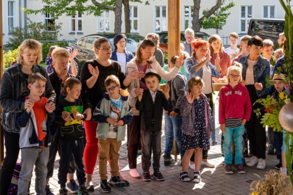 Eine Gruppe von Kindern und Erwachsenen steht lächelnd zusammen im Freien.