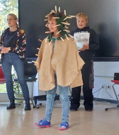 Ein Kind trägt ein Kostüm mit Klammern und steht vor zwei anderen Personen.