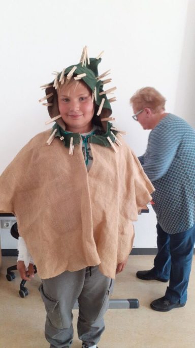 Kind in einem auffälligen Kostüm mit Stacheln, daneben eine Person am Tisch.