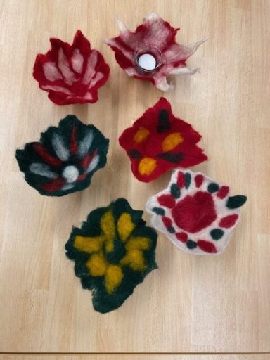 Sechs farbenfrohe gefilzte Schalen in Rot, Grün, Gelb und Weiß auf einem Holztisch.