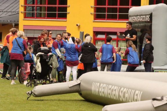 Gruppenevent im Freien mit Menschen in blauen und roten Westen, einem großen aufblasbaren Objekt.