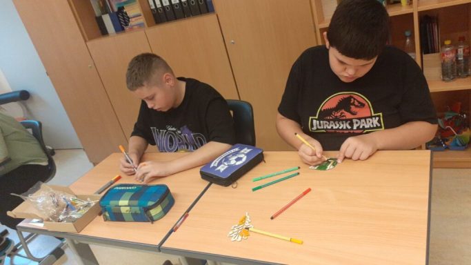 Zwei Kinder zeichnen und basteln an einem Tisch in einem Klassenzimmer.