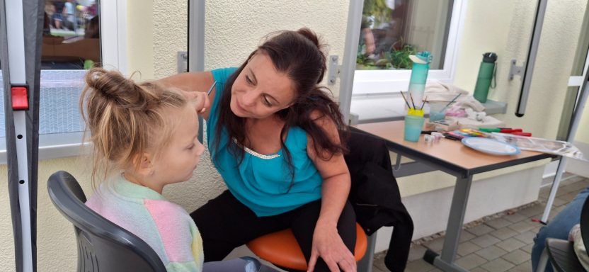 Frau spricht mit einem Kind in einem Raum mit Tischen und Stühlen.