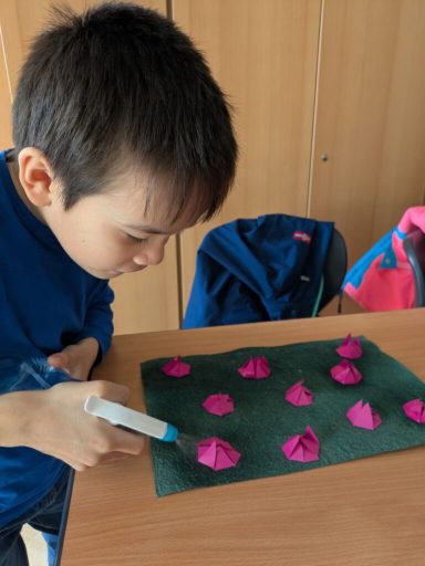 Ein Junge formt rosa Kneteblumen auf einem grünen Untergrund.