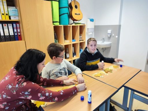 Drei Personen, darunter ein Lehrer, arbeiten an einem Tisch mit Bastelmaterialien.