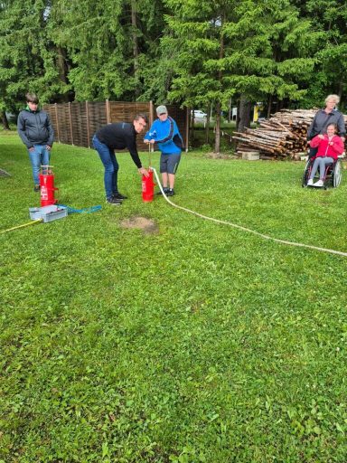 Grupp von Personen im Freien, einige arbeiten mit Feuerlöschern auf Rasenfläche.