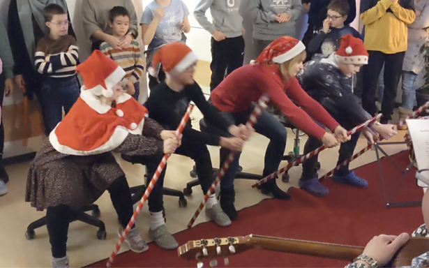 Vier Personen in Weihnachtsmützen ziehen an einem Seil, umgeben von Zuschauern.