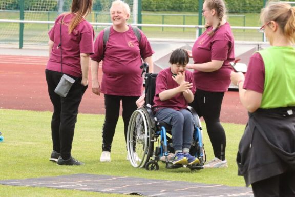 Fünf Personen, darunter ein Junge im Rollstuhl, stehen auf einem Sportplatz.
